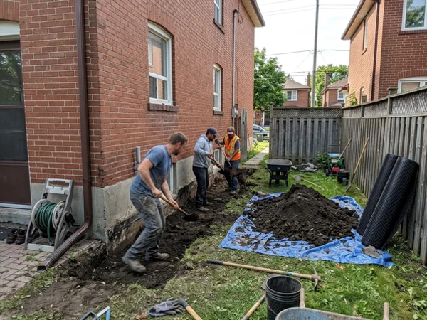 Three-person crew excavating beside a red brick semi to expose the foundation