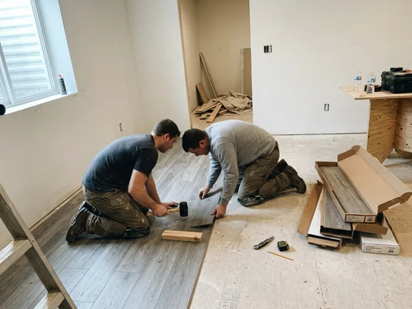 Two crew members laying waterproof luxury vinyl plank in a rebuilt basement rec room