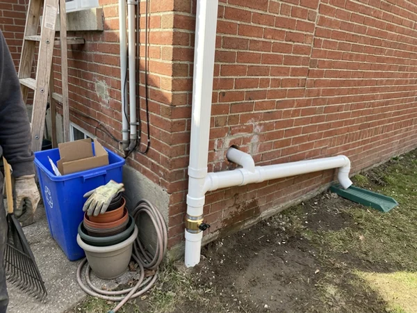 New PVC discharge line with check valve exiting through a brick wall
