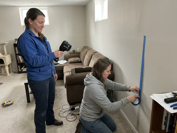 Technicians scanning drywall with a thermal imaging camera and taping the wet line