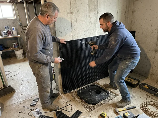 Two technicians fitting dimple drainage membrane above a new sump pit