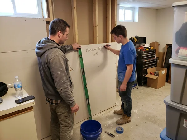 Two technicians marking a flood cut line and moisture readings on drywall